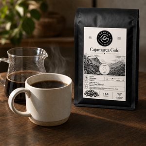 Cajamarca Gold coffee bag with steaming brewed coffee and glass server