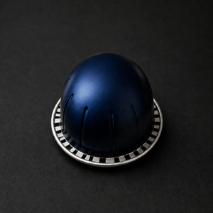 Close-up of an unbranded navy Vertuo-compatible coffee capsule with domed shape and fluted sides